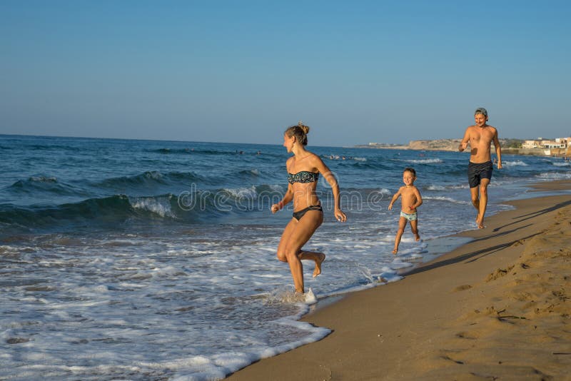 Mãe de sorriso feliz, pai e seus jogo e corredor do filho na praia Conceito da família amigável Dias de verão felizes foto de stock Mãe de sorriso feliz, pai e seus jogo e corredor do filho na praia Conceito da família amigável Dias de verão felizes foto de stock