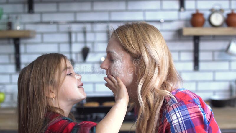 Mãe despreocupada e filha novas que enganam na cozinha A mamã e a criança têm o divertimento junto