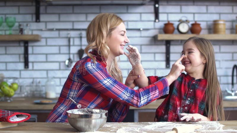 Mãe despreocupada e filha novas que enganam na cozinha que cozinha na mesa de cozinha A mamã e a criança têm o divertimento junto