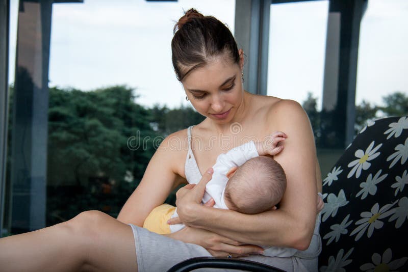 Mãe do amor que nutre o filho pequeno e que senta-se no vestido na cadeira de plataforma do alinhador longitudinal da flor na fre imagem de stock Mãe do amor que nutre o filho pequeno e que senta-se no vestido na cadeira de plataforma do alinhador longitudinal da flor na fre imagem de stock