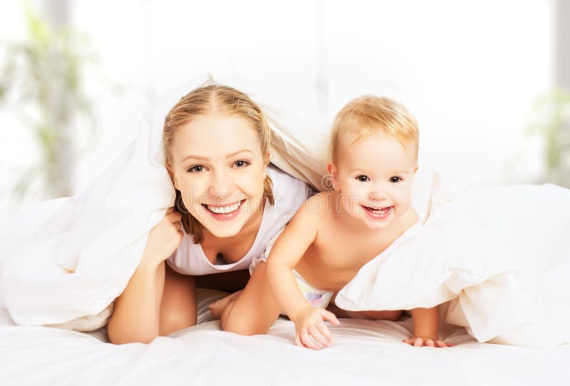 Mãe e bebê felizes da família sob coberturas na cama foto de stock royalty free Mãe e bebê felizes da família sob coberturas na cama foto de stock royalty free