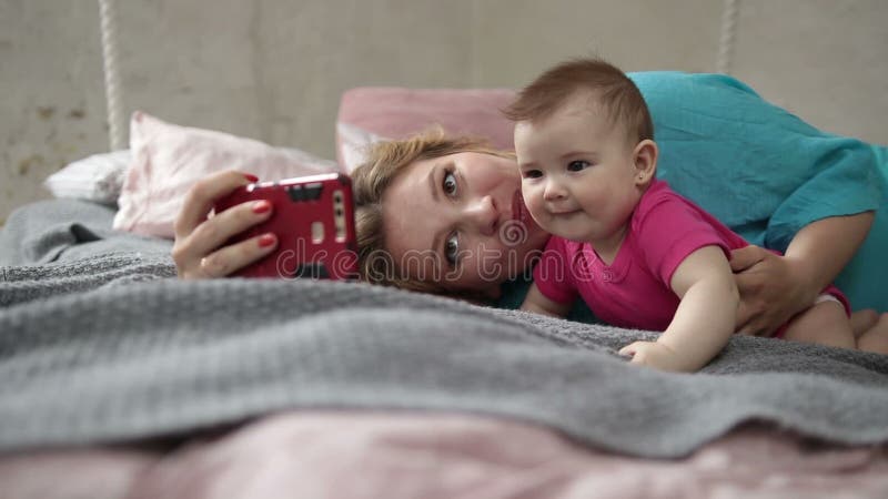 Mãe e bebê que tomam o selfie com o telefone na cama