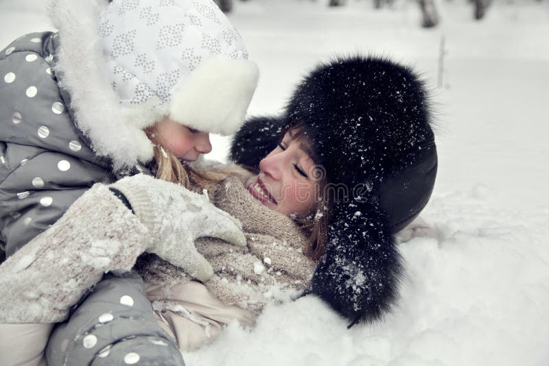 A mãe e a filha atrativas da família colocam em uma neve em um parque do inverno fotografia de stock royalty free A mãe e a filha atrativas da família colocam em uma neve em um parque do inverno fotografia de stock royalty free
