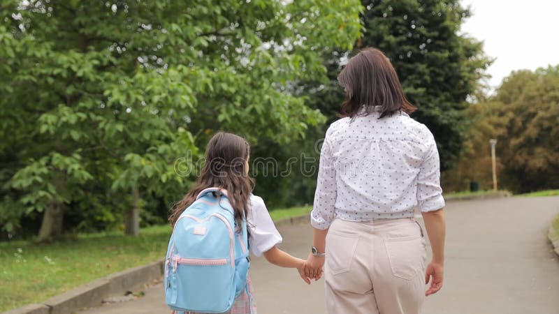 Mãe e filha caminham pelo caminho do asfalto no parque de mãos dadas. estão a gozar férias conjuntas na natureza