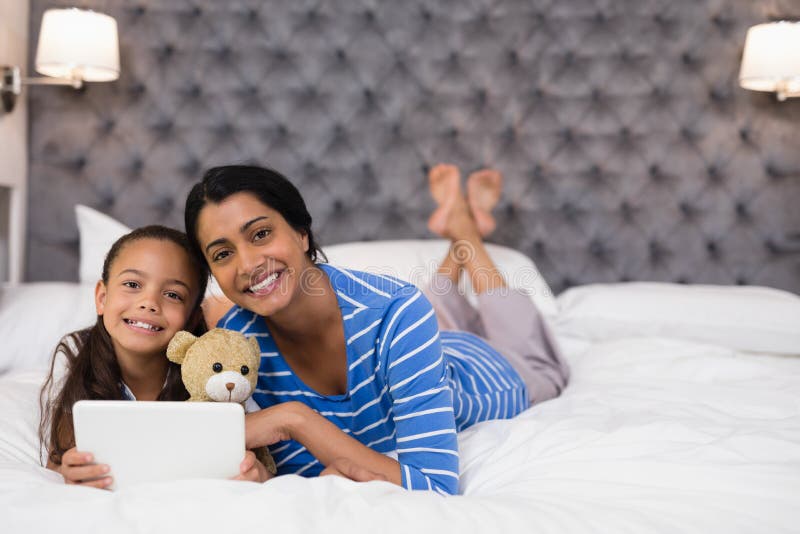 Mãe e filha de sorriso que usa a tabuleta digital ao encontrar-se na cama em casa fotografia de stock Mãe e filha de sorriso que usa a tabuleta digital ao encontrar-se na cama em casa fotografia de stock