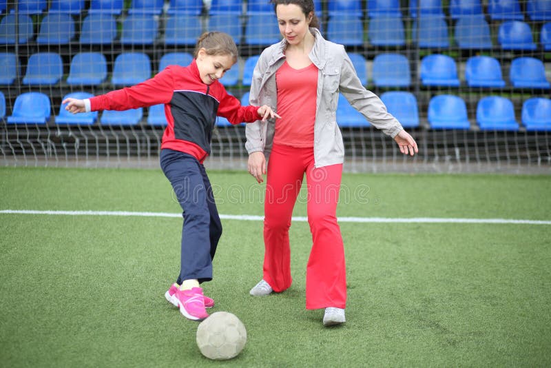 Mãe e filha em trajes correndo com a bola no estádio