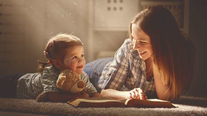 A mãe e a filha felizes da família leram um livro na noite