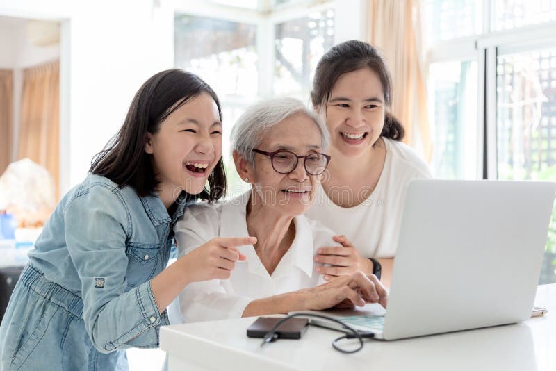 Mãe e filha que surfam o Internet; olhando algo interessante com avó, quando superior asiático de sorriso feliz da mulher imagem de stock royalty free Mãe e filha que surfam o Internet; olhando algo interessante com avó, quando superior asiático de sorriso feliz da mulher imagem de stock royalty free