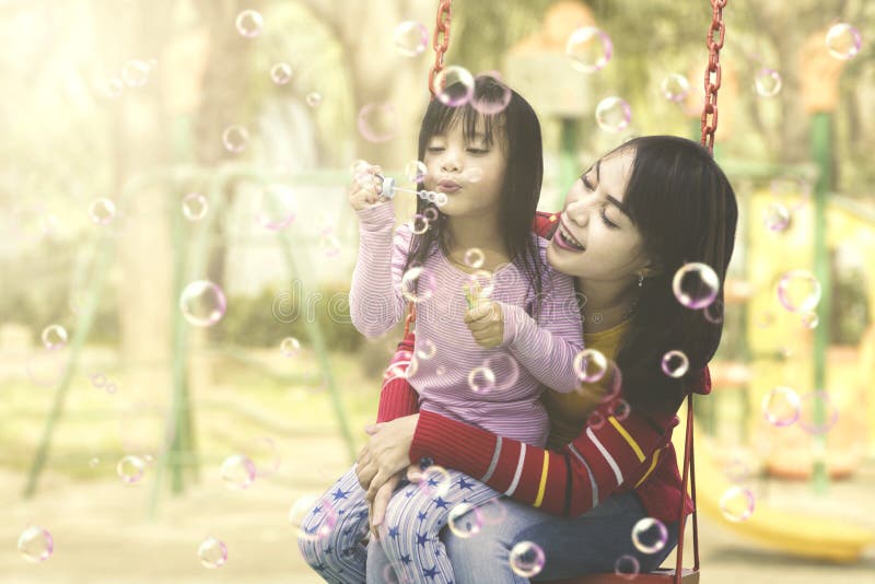 Mãe e filha que têm o divertimento com bolhas de sabão no campo de jogos fotografia de stock Mãe e filha que têm o divertimento com bolhas de sabão no campo de jogos fotografia de stock