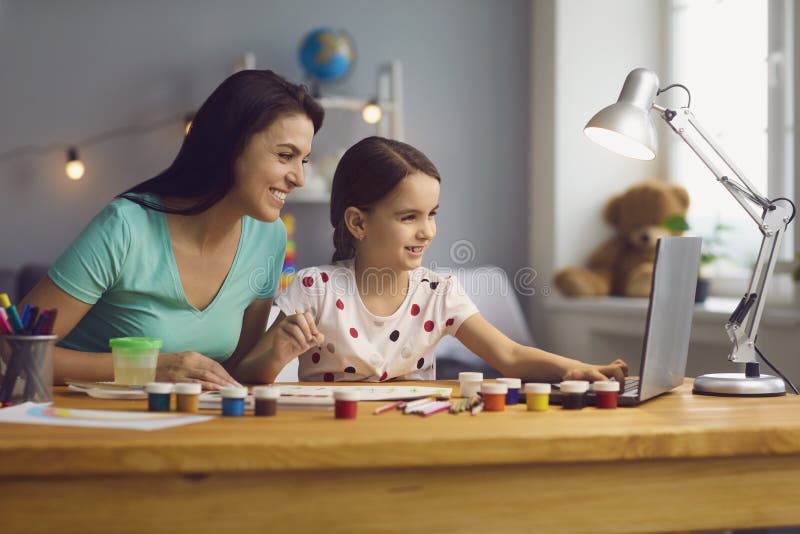 Mãe feliz ajudando sua filha fofa a estudar online em casa. aula de arte para pais e crianças juntas no laptop
