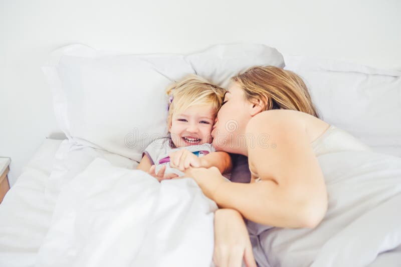 Mãe feliz e loving que tem o divertimento e que beija sua filha na cama Conceito da manhã da família Passando o tempo livre junto foto de stock Mãe feliz e loving que tem o divertimento e que beija sua filha na cama Conceito da manhã da família Passando o tempo livre junto foto de stock