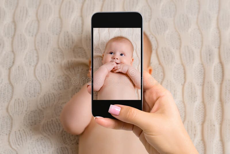 Mãe feliz que toma uma imagem de seu bebê na ucha com telefone esperto fotografia de stock Mãe feliz que toma uma imagem de seu bebê na ucha com telefone esperto fotografia de stock