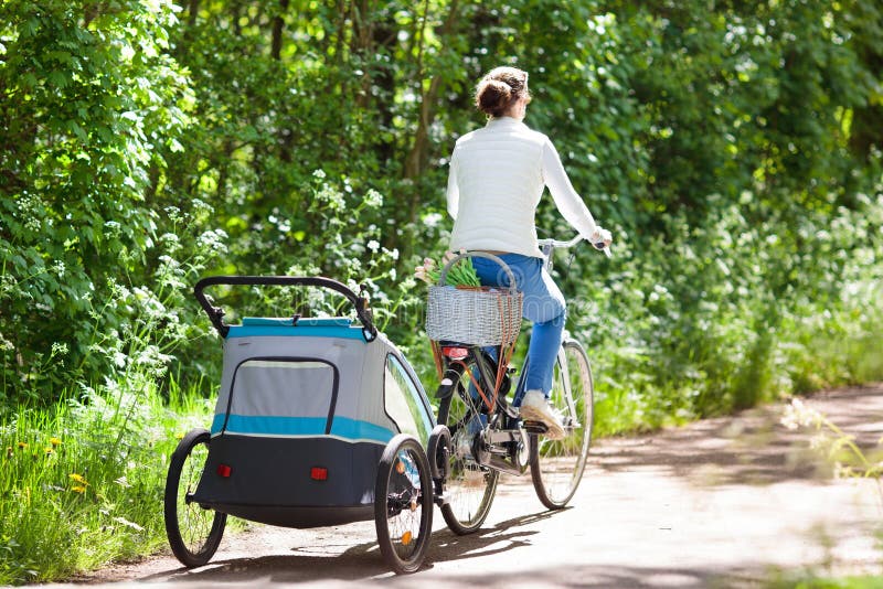 Mãe na bicicleta com o reboque da bicicleta do bebê no parque imagem de stock Mãe na bicicleta com o reboque da bicicleta do bebê no parque imagem de stock