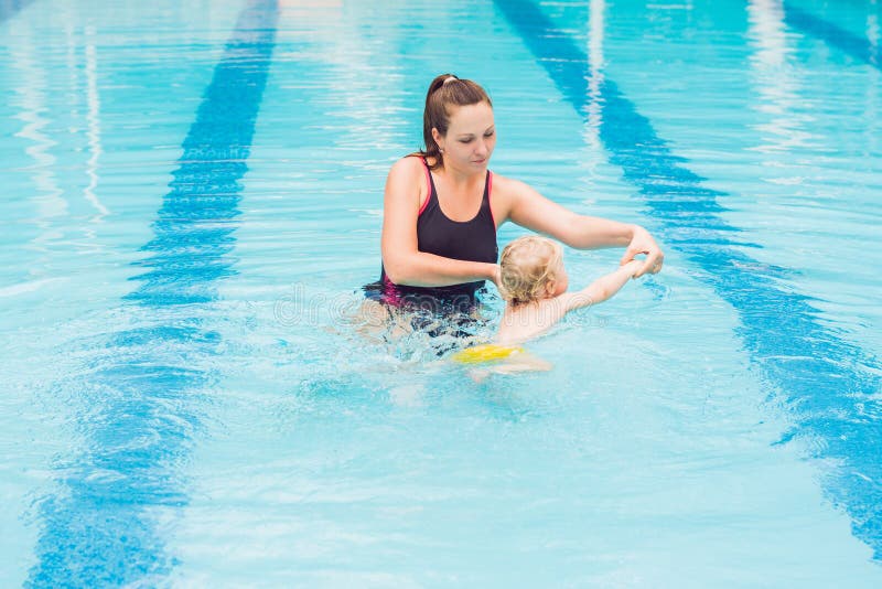 A mãe nova ensina seu filho pequeno, como nadar em uma piscina foto de stock A mãe nova ensina seu filho pequeno, como nadar em uma piscina foto de stock