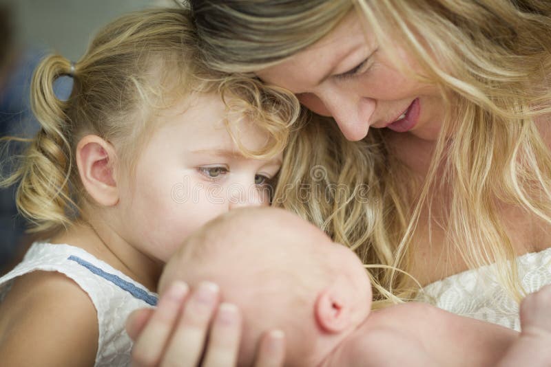 A mãe nova guarda o bebê recém-nascido como a irmã nova Looks imagens de stock A mãe nova guarda o bebê recém-nascido como a irmã nova Looks imagens de stock