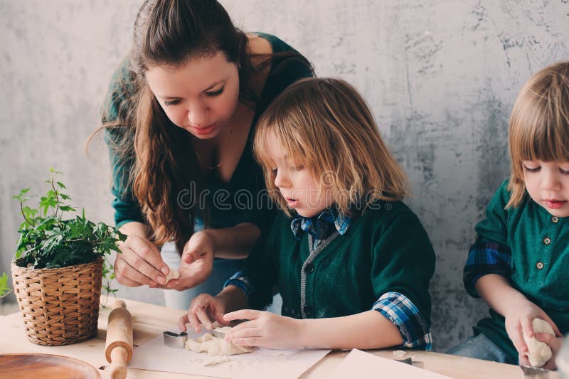 Mãe que cozinha com as crianças na cozinha Irmãos da criança que cozem junto e que jogam com pastelaria em casa imagem de stock royalty free Mãe que cozinha com as crianças na cozinha Irmãos da criança que cozem junto e que jogam com pastelaria em casa imagem de stock royalty free