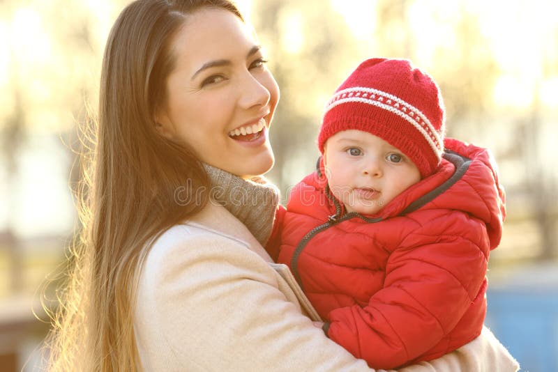 Portrait of a smiley mother posing with her baby keeping warm wearing a red jacket outdoors in winter. Portrait of a smiley mother posing with her baby keeping warm wearing a red jacket outdoors in winter