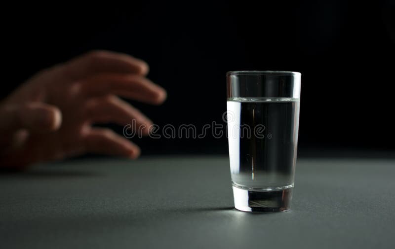 A mão alcança para um vidro da bebida da vodca ou do álcool fotografia de stock A mão alcança para um vidro da bebida da vodca ou do álcool fotografia de stock