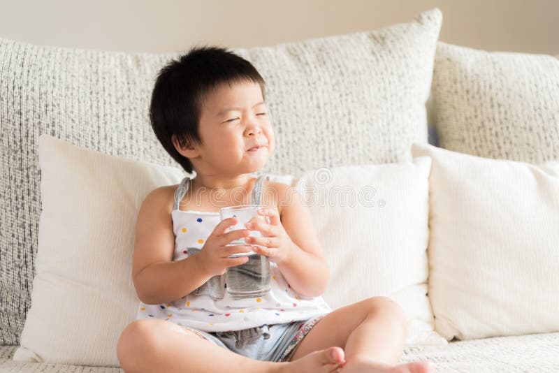 Mão asiática pequena feliz da menina que guarda o vidro de água potável imagem de stock Mão asiática pequena feliz da menina que guarda o vidro de água potável imagem de stock