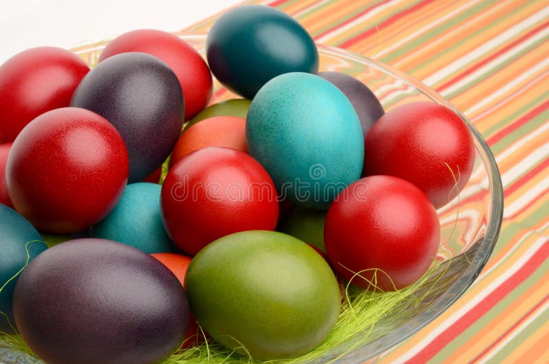 A mão colorida tingiu ovos da páscoa em uma bacia em uma tabela com toalha de mesa listrada. fotografia de stock royalty free A mão colorida tingiu ovos da páscoa em uma bacia em uma tabela com toalha de mesa listrada. fotografia de stock royalty free