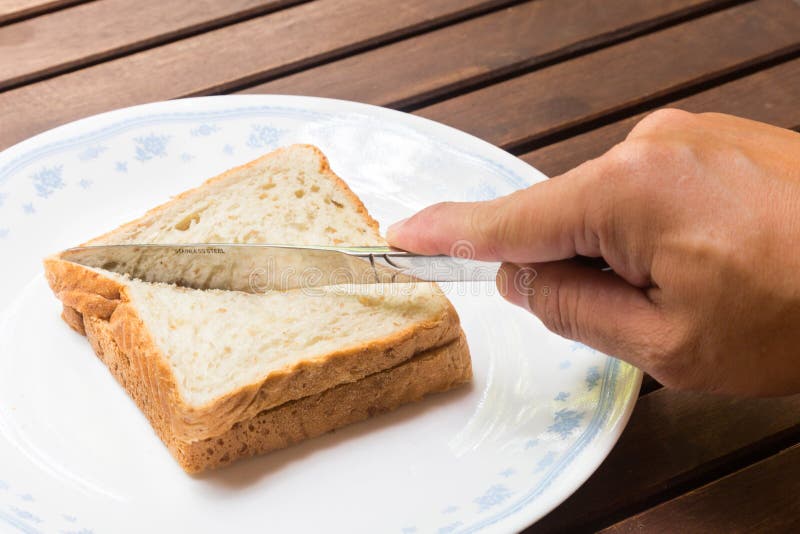 Hand with knife slicing wholemeal sandwich bread diagonally into two portions. Hand with knife slicing wholemeal sandwich bread diagonally into two portions.