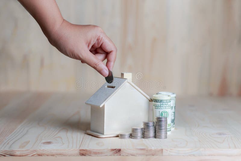 Mão da mulher que põe a moeda dentro ao financ de madeira do mealheiro da casa foto de stock Mão da mulher que põe a moeda dentro ao financ de madeira do mealheiro da casa foto de stock