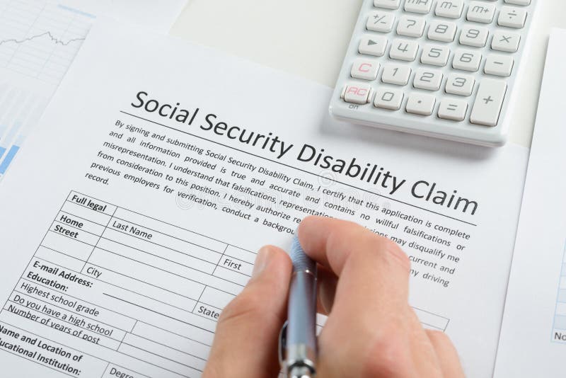Mão da pessoa com a pena que enche o formulário da inabilidade da segurança social foto de stock Mão da pessoa com a pena que enche o formulário da inabilidade da segurança social foto de stock