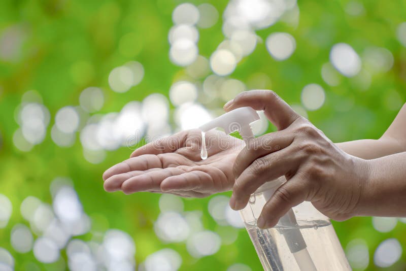 The woman`s hand is pressing the hand wash gel for the protection against coronary virus or Covid-19 and the green nature background blurred with the concept of health care and disease prevention. The woman`s hand is pressing the hand wash gel for the protection against coronary virus or Covid-19 and the green nature background blurred with the concept of health care and disease prevention