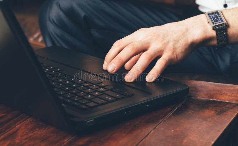 A mão de um homem com um relógio de pulso está no touchpad do portátil O homem de negócios trabalha em casa em sua própria sala imagem de stock A mão de um homem com um relógio de pulso está no touchpad do portátil O homem de negócios trabalha em casa em sua própria sala imagem de stock