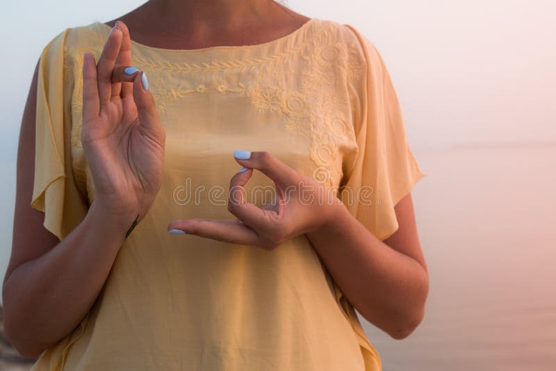 Mão de uma mulher que medita em uma pose da ioga na praia no por do sol fotografia de stock Mão de uma mulher que medita em uma pose da ioga na praia no por do sol fotografia de stock