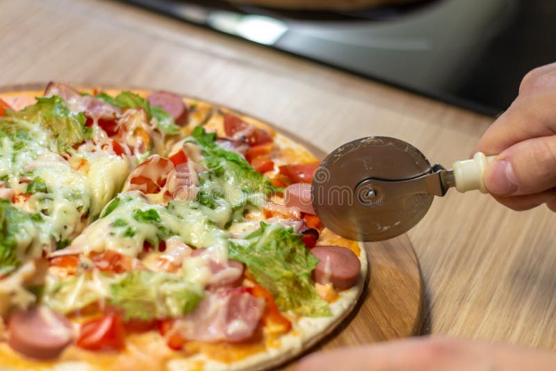 Mão do close up do padeiro do cozinheiro chefe no uniforme branco que corta a pizza na cozinha, foco seletivo macio foto de stock Mão do close up do padeiro do cozinheiro chefe no uniforme branco que corta a pizza na cozinha, foco seletivo macio foto de stock