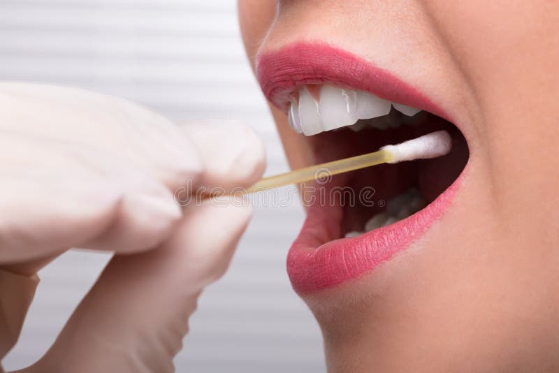 A mão do dentista que toma o teste da saliva da boca da mulher