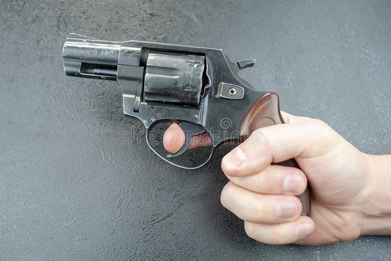 A mão do homem que mantém um revólver contra um fundo cinzento, dedo no disparador fotos de stock A mão do homem que mantém um revólver contra um fundo cinzento, dedo no disparador fotos de stock