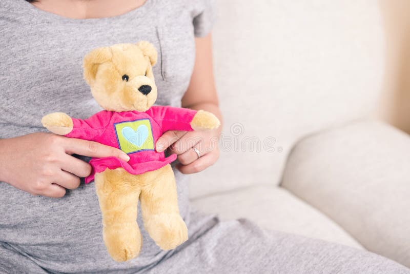 Mão feliz da mulher gravida que guarda a boneca do urso de peluche em sua barriga w fotografia de stock Mão feliz da mulher gravida que guarda a boneca do urso de peluche em sua barriga w fotografia de stock