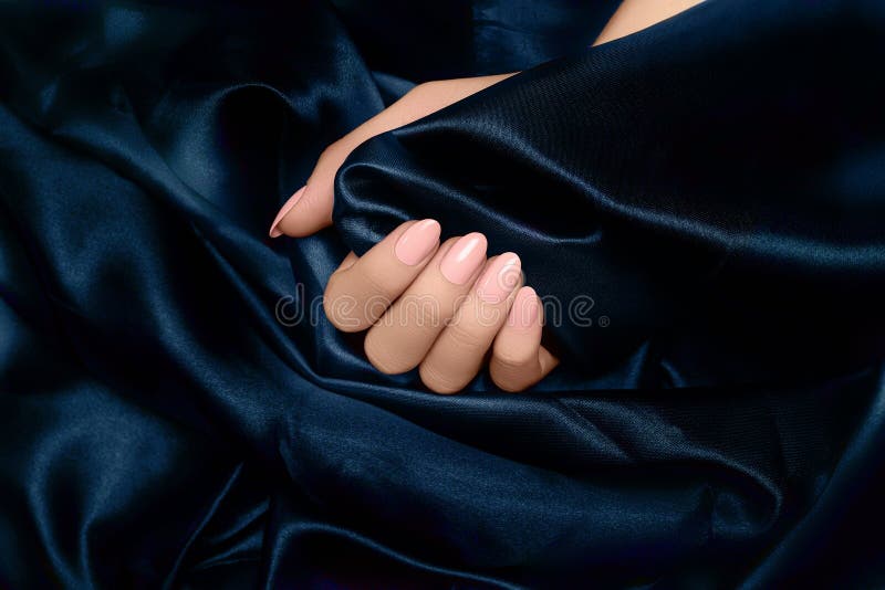 Mão feminina com desenho de unhas rosa. manicura de esmalte roxa. mão da mulher sobre o fundo do tecido azul