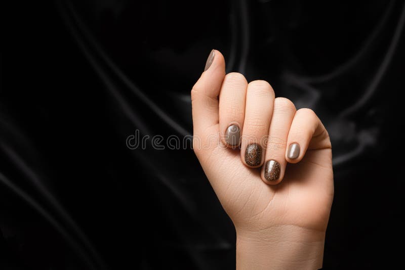 Mão fêmea com desenho de pregos castanhos. manicura de esmalte marrom. mão da mulher sobre o fundo do tecido negro