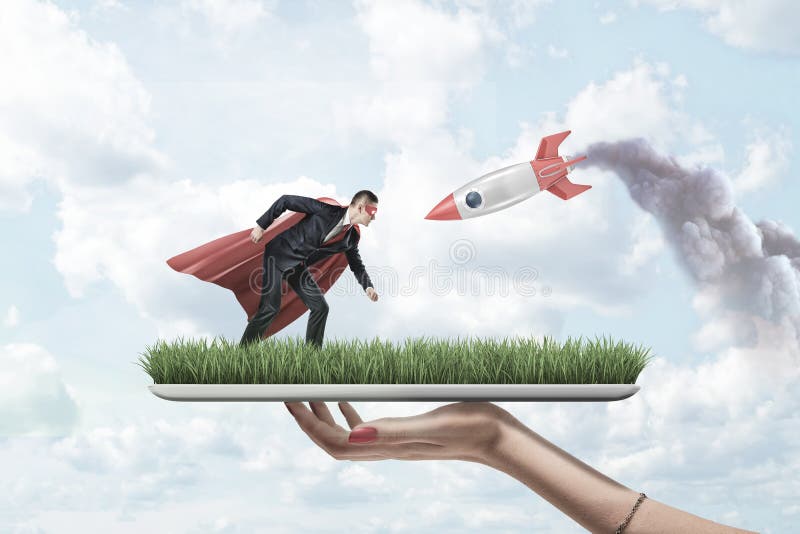 M?o f?mea que guarda a placa da grama com o homem de neg?cios pequeno na m?scara vermelha do superman e o casaco com o foguete ve fotografia de stock royalty free M?o f?mea que guarda a placa da grama com o homem de neg?cios pequeno na m?scara vermelha do superman e o casaco com o foguete ve fotografia de stock royalty free