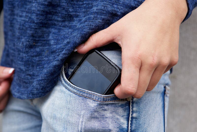 A mão fêmea que remove o telefone celular de suas calças de brim pocket foto de stock A mão fêmea que remove o telefone celular de suas calças de brim pocket foto de stock