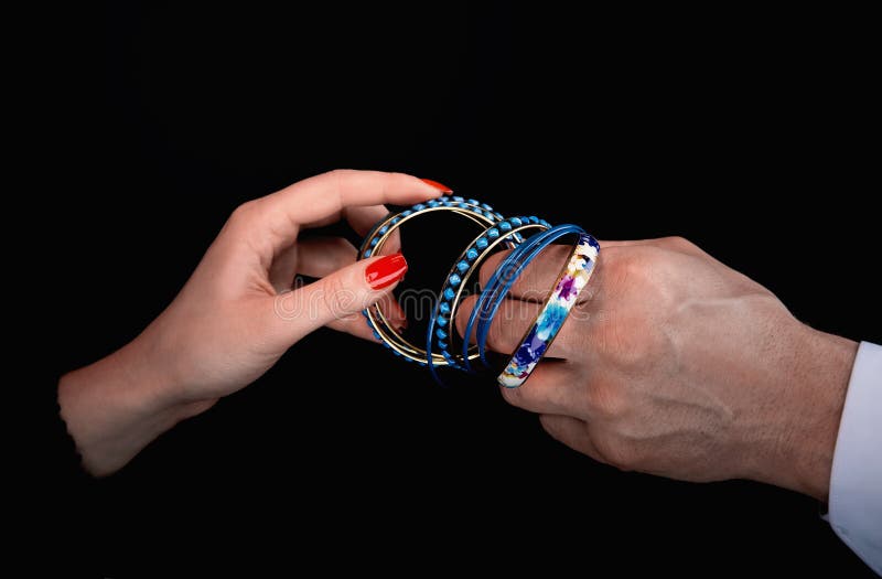 Men`s hand giving blue bracelet to woman`s hands in a black background. Men`s hand giving blue bracelet to woman`s hands in a black background