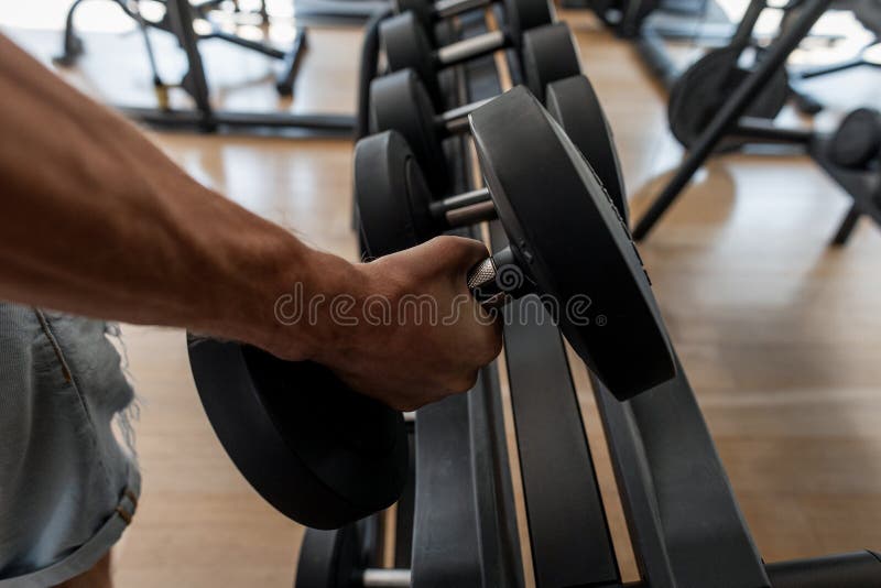 Mão masculina forte que levanta um peso em um estúdio dos esportes Trens atléticos do homem novo no gym Close-up de uma m?o do ` imagem de stock royalty free Mão masculina forte que levanta um peso em um estúdio dos esportes Trens atléticos do homem novo no gym Close-up de uma m?o do ` imagem de stock royalty free