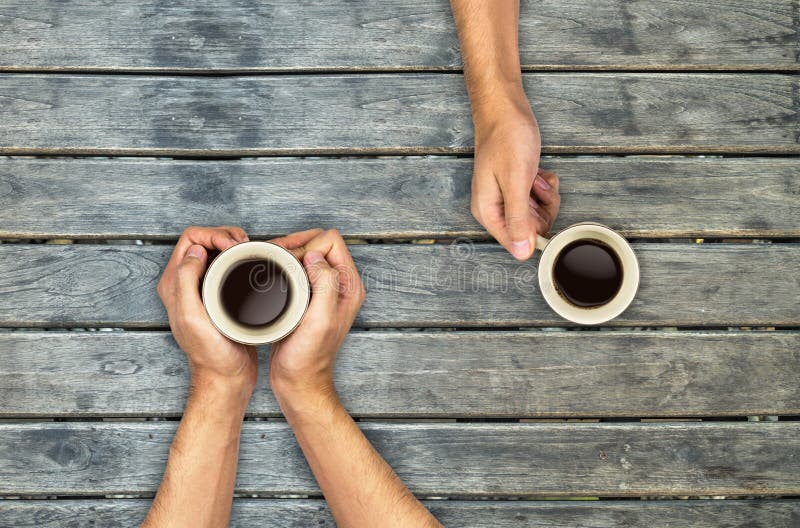 Mãos das canecas de café que guardam sobre a tabela de madeira imagens de stock Mãos das canecas de café que guardam sobre a tabela de madeira imagens de stock