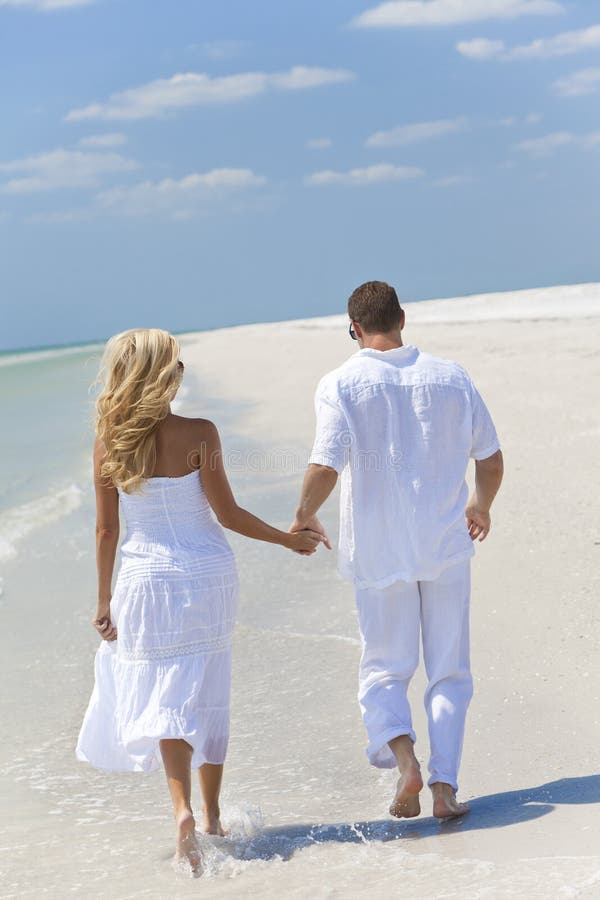 Mãos de passeio da terra arrendada dos pares novos felizes na praia foto de stock Mãos de passeio da terra arrendada dos pares novos felizes na praia foto de stock