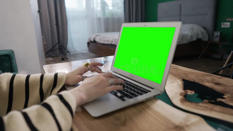 Mãos de uma mulher digitando em um laptop com tela verde
