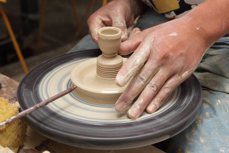 Close-up view of potter's hands shaping a clay candlestick on a spinning wheel in an Asian pottery. Close-up view of potter's hands shaping a clay candlestick on a spinning wheel in an Asian pottery.