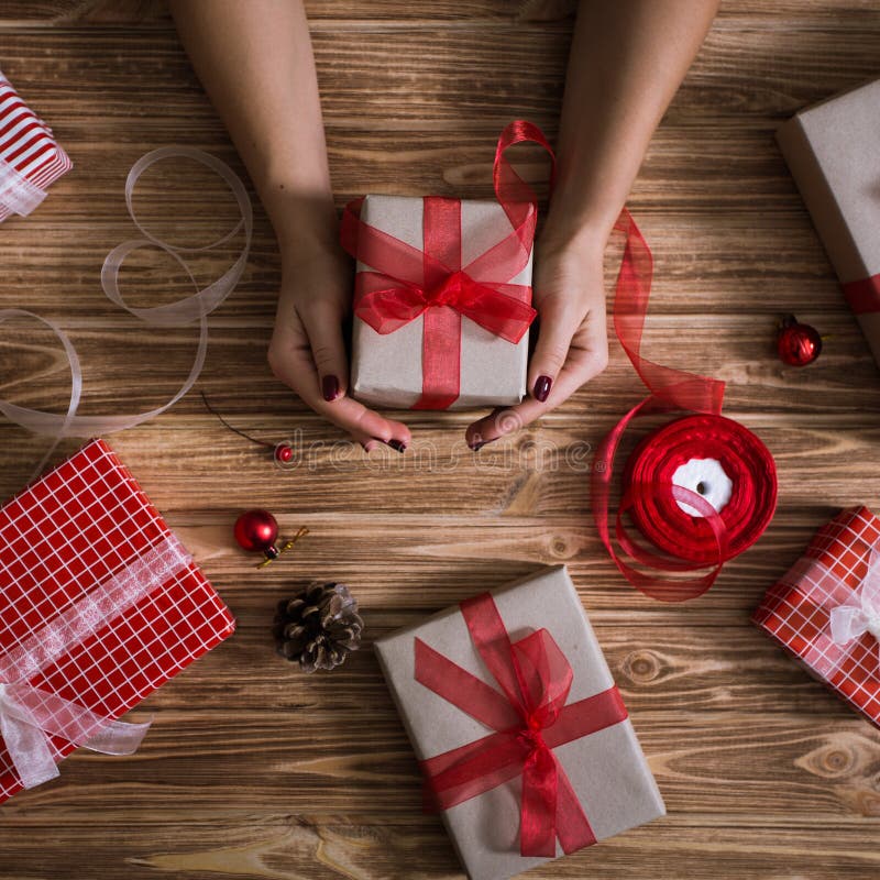 Mãos fêmeas que envolvem presentes do xmas no papel e que amarram os acima com as linhas vermelhas e do branco imagem de stock royalty free Mãos fêmeas que envolvem presentes do xmas no papel e que amarram os acima com as linhas vermelhas e do branco imagem de stock royalty free