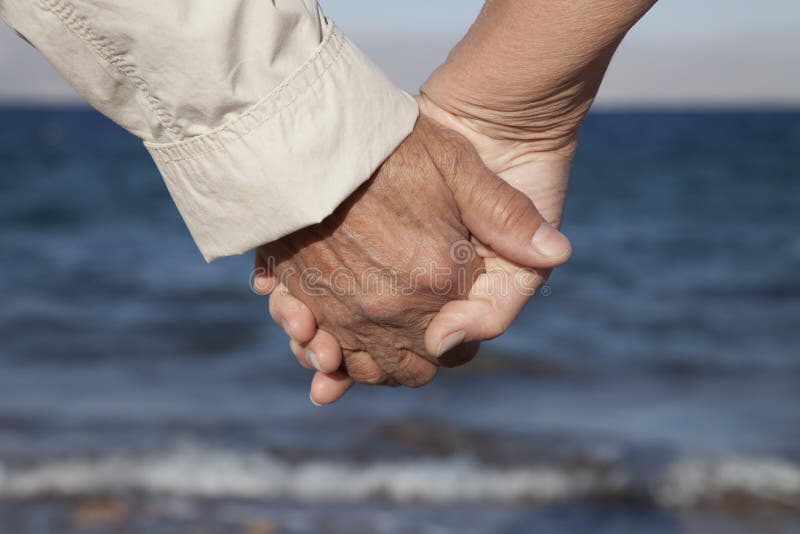 Mãos sênior da terra arrendada dos pares na praia foto de stock Mãos sênior da terra arrendada dos pares na praia foto de stock