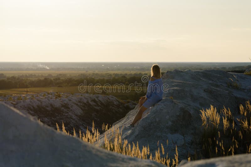 Girl on a mountain in a blue dress watches the sunset. The girl contemplates the evening landscape. Girl on a mountain in a blue dress watches the sunset. The girl contemplates the evening landscape