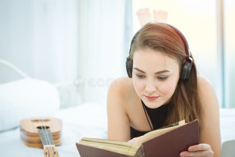 Mädchen, das auf Bettlesebuch liegt und Musik auf Kopfhörern hört lizenzfreie stockbilder Mädchen, das auf Bettlesebuch liegt und Musik auf Kopfhörern hört lizenzfreie stockbilder