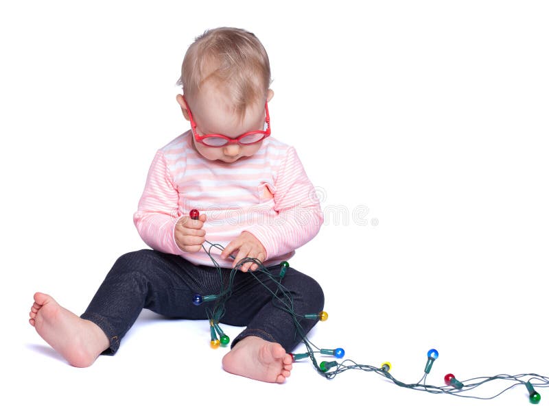 Mädchen, das auf weißem Hintergrund sitzt und mit Weihnachtslichtern spielt lizenzfreies stockfoto