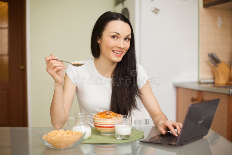Mädchen, das frühstückt und ihren Laptop in der Küche verwendet stockbilder Mädchen, das frühstückt und ihren Laptop in der Küche verwendet stockbilder